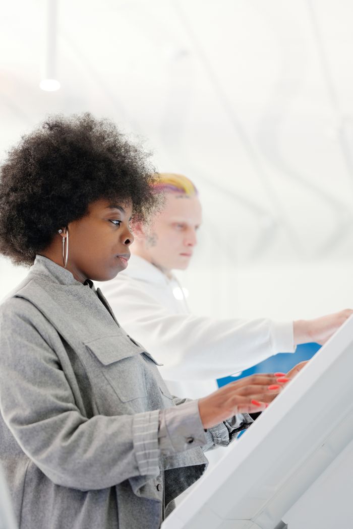 Side view of a stylish woman with afro hair using a touchscreen indoors.
